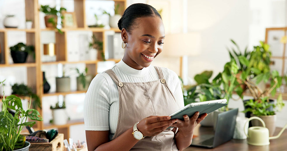 Jeune femme souriante entourée de verdure qui recherche en ligne sur sa tablette