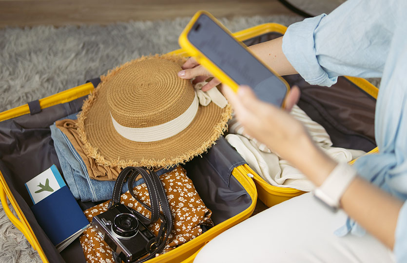 Femme préparant soigneusement les essentiels pour ses vacances dans une valise jaune, en organisant ses documents de voyage, un chapeau élégant, un appareil photo et ses vêtements, en vue d’un voyage passionnant.