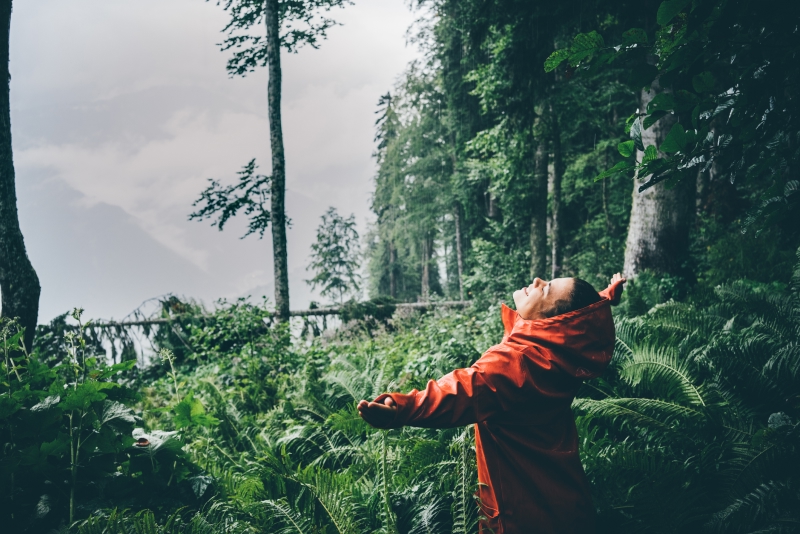 Une jeune femme en imperméable sourit sous la pluie
