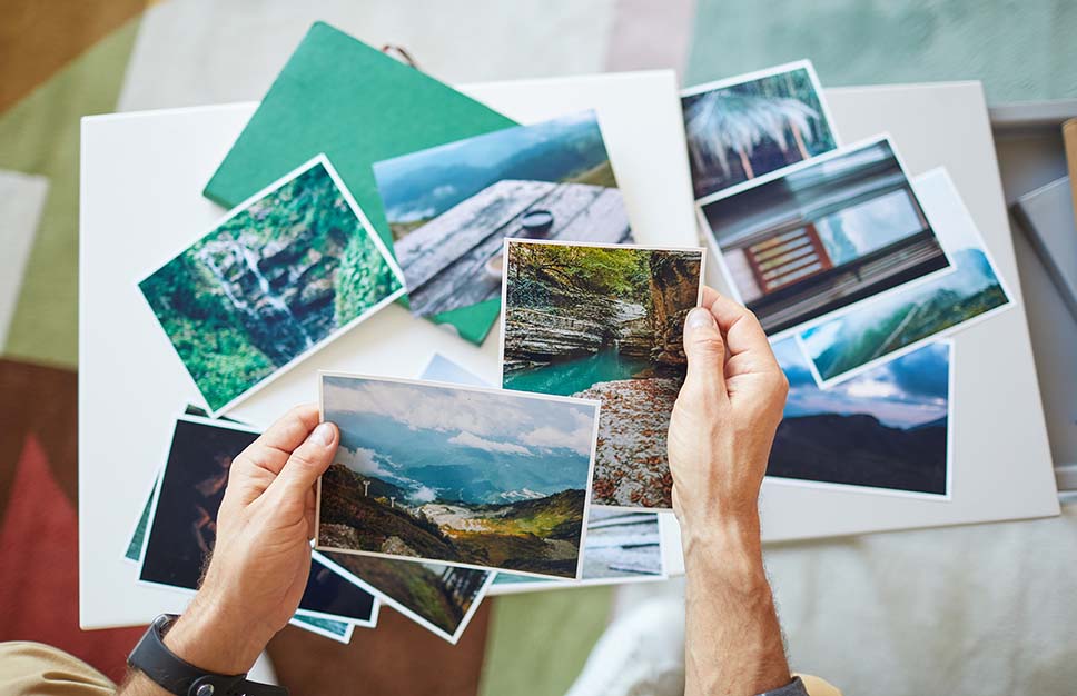 Mains sélectionnant des photos souvenirs d’un voyage récent pour créer un montage. 