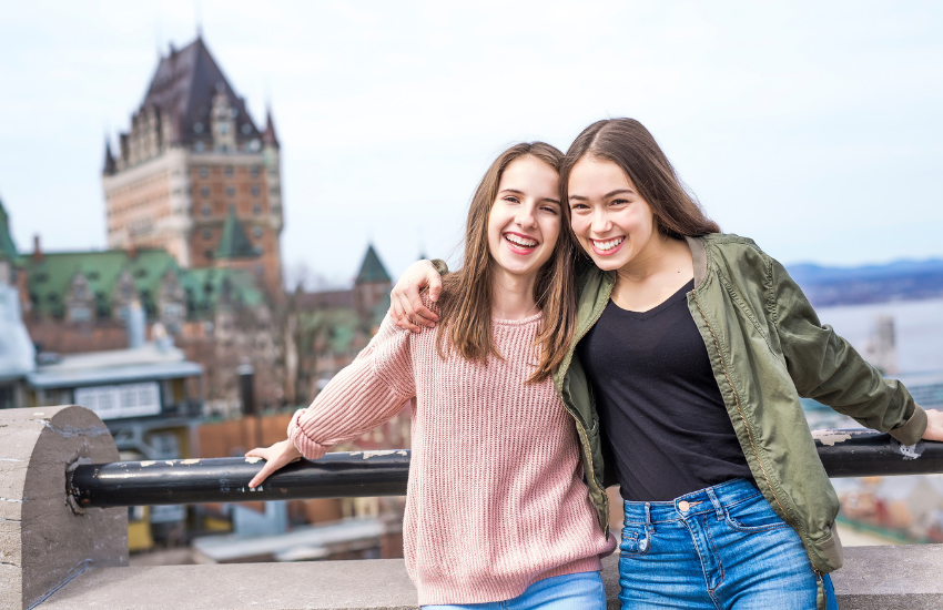 Deux personnes appuyées contre une balustrade surplombant le Vieux‑Québec, avec le Château Frontenac et le fleuve Saint‑Laurent en arrière‑plan. 