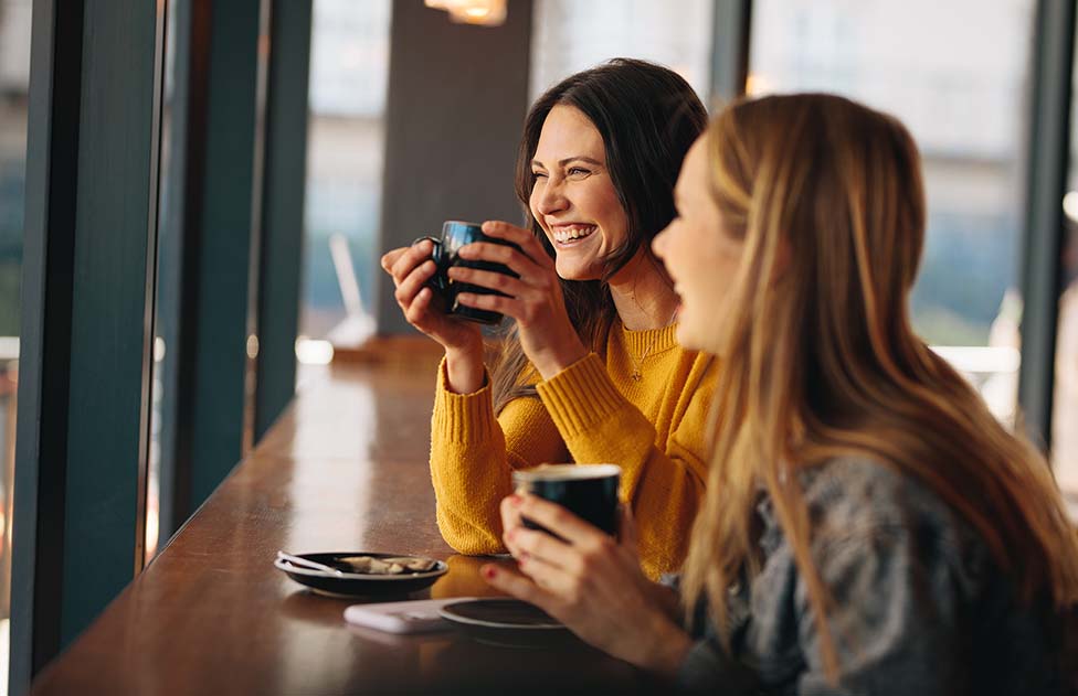 Deux bonnes amies souriantes partageant un café et heureuses de se retrouver après les vacances. 