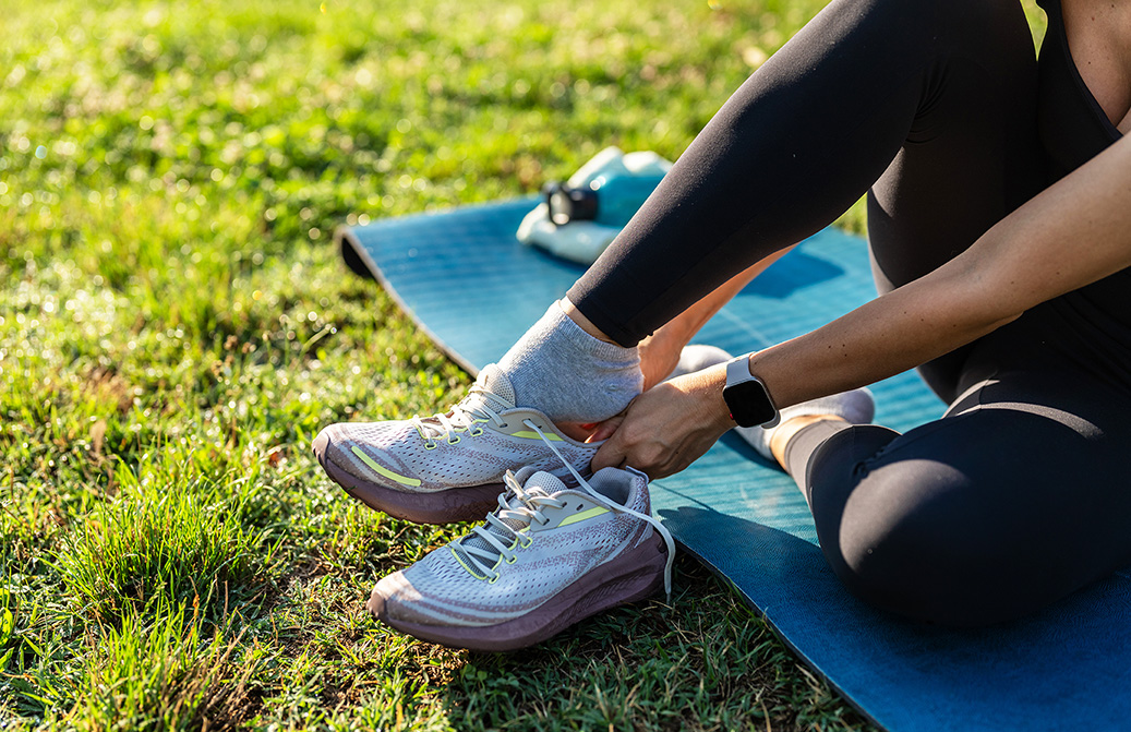 Jeune femme sportive assise sur un tapis de yoga dans un parc, attachant ses lacets après une séance d’entraînement. 