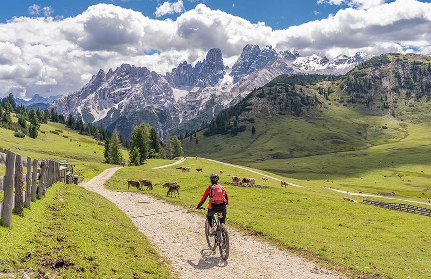 Femme mature active faisant du vélo de montagne électrique sur le haut plateau de Prato Piazza, dans les Dolomites des Trois Cimes, avec la silhouette rocheuse du mont Cristallo en arrière-plan, dans le Tyrol du Sud, en Italie. 