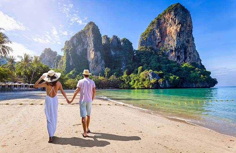 Un couple heureux marche sur la plage de Railay, à Krabi, en Thaïlande, avec en toile de fond des eaux turquoise et une forêt tropicale verdoyante.